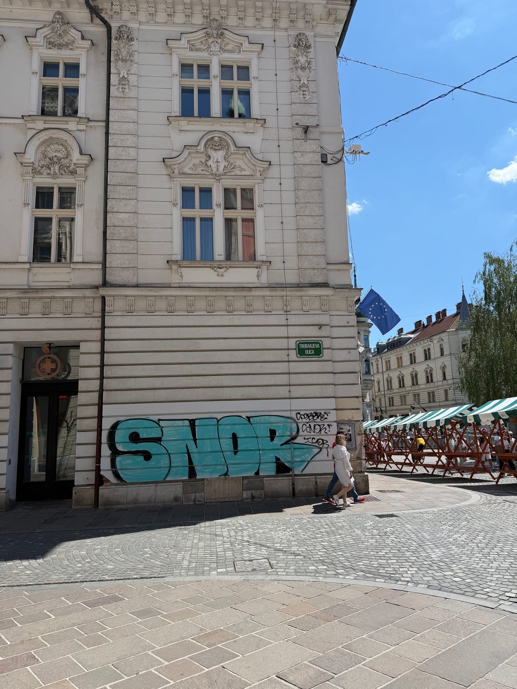Velik turkizen podpis SNOR čez pritličje okrašene stavbe v središču Ljubljane.