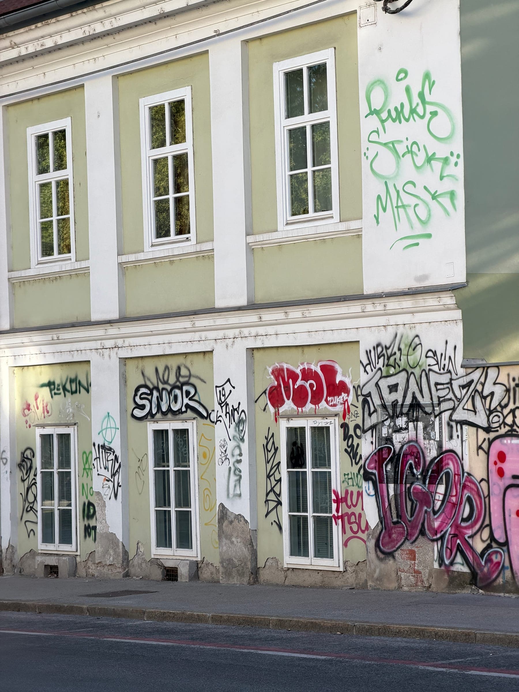 Podpis SNOR in drugi grafiti prekrivajo svetlo zeleno fasado na Rozmanovi ulici ter segajo tudi v nadstropje.
